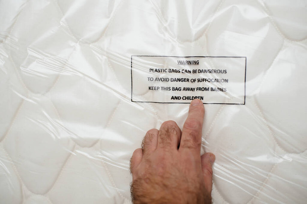 POV männliche Hand zeigt Matratze entboxende Hand zeigt auf Warnung - Plastiktüten können für Kinder gefährlich sein Erstickungsgefahr - Foto, Bild