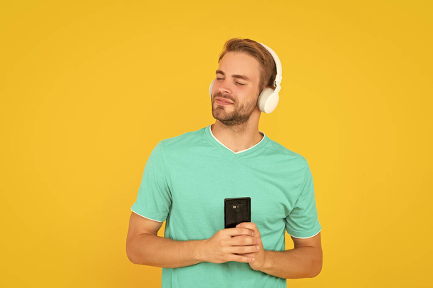 Happy young man enjoy listening to music on mobile phone with headphones yellow background, leisure. - Fotoğraf, Görsel