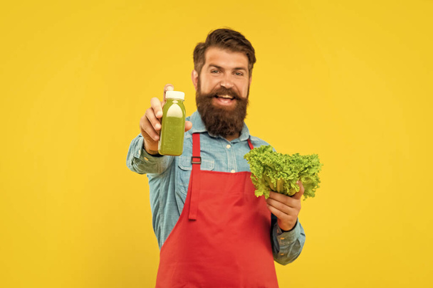 Happy man giving juice bottle holding fresh lettuce yellow background, juice shopkeeper. - Foto, Imagem