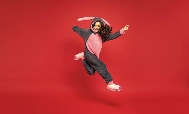 amazed kid in comfortable pajama jumping on red background, full length, comfort. - Фото, зображення