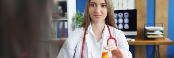Portret kobiety lekarza daje pacjentowi plastikowy pojemnik wypełniony lekami, stażysta reklamuje pigułki na szybszą regenerację. Zdrowie, koncepcja apteki - Zdjęcie, obraz