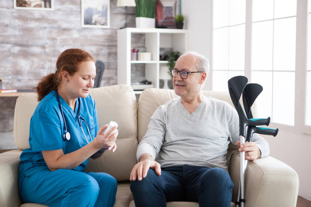 看護婦の家で松葉杖を持った陽気な上級男性に話す女性の介護テイカー - 写真・画像