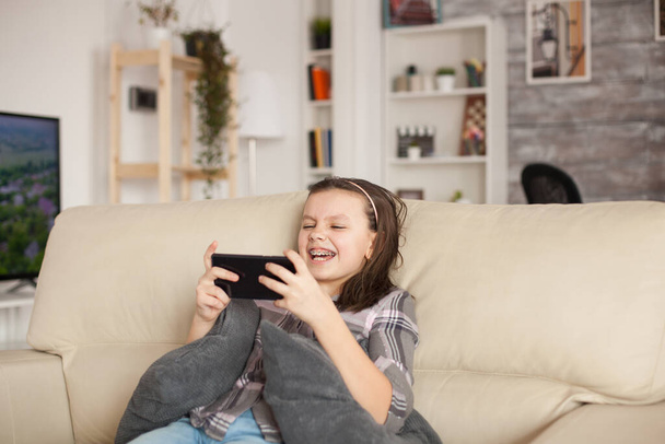 Happy little girl playing games on smartphone - Фото, изображение