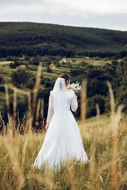 záběr krásné nevěsty v bílých šatech uprostřed přírody, nevěsta drží krásnou kytici - Fotografie, Obrázek
