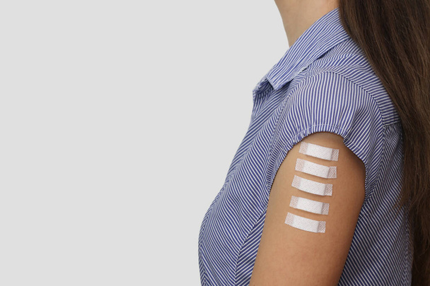 Πέντε ιατρικά έμπλαστρα στο χέρι μιας νεαρής γυναίκας. Σύμβολο πέντε δόσεων εμβολίων covid-19, συμπεριλαμβανομένων των αναμνηστικών εμβολίων. Ελεύθερος χώρος για κείμενο σε γκρι φόντο. Χώρος για ένα σύντομο κείμενο σε διορθώσεις. - Φωτογραφία, εικόνα