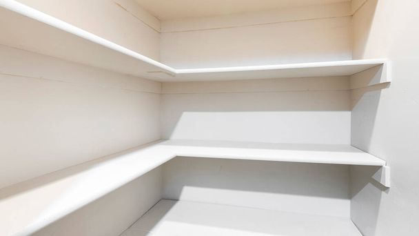 Panorama White linen closet with wall mounted shelves and carpeted floor. Narrow walk-in closet with built-in shelves on the front and right walls. - Foto, afbeelding