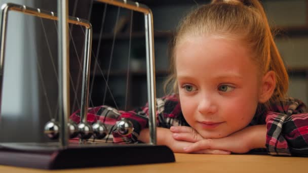 Cute little child toddler beautiful young restful school girl sit on psychotherapy session indoors pretty blonde kid daughter looking at magnetic swinging metal steel balls calm down therapy hypnosis - Footage, Video