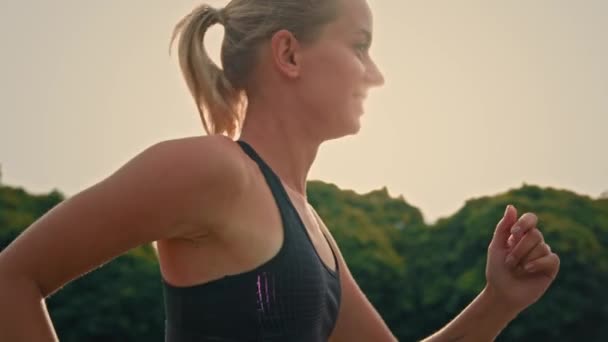 Side view athletic girl sportswoman runner jogger active fit γυναίκα τρέχει στο δρόμο της πόλης προπόνηση ταχύτητα αντοχής τρέξιμο στις ακτίνες του ήλιου πρωί πρακτική άσκηση καρδιο αθλητισμού για αγώνα ή μαραθώνιο - Πλάνα, βίντεο