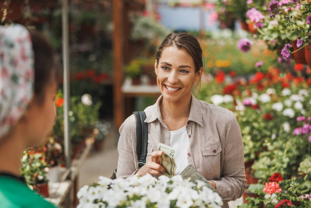 Een jonge vrouw kopen potted van jonge vrouw ondernemer in een tuin centrum. - Foto, afbeelding