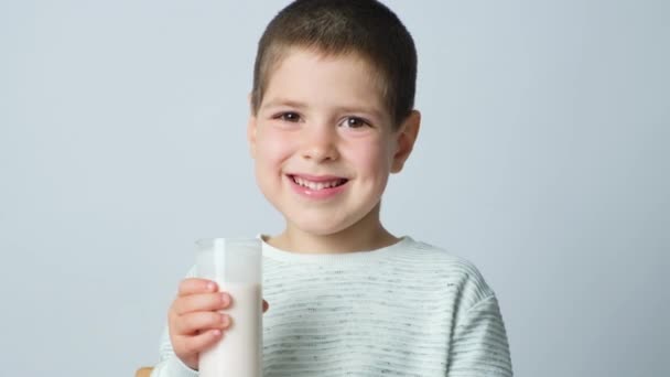 Een knappe 5-jarige jongen houdt een glas gefermenteerde melk in een glas op een witte achtergrond. - Video