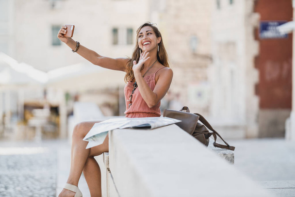 Shot na mladé veselá žena brát selfie se svým smartphonem při turné v cizím městě. - Fotografie, Obrázek