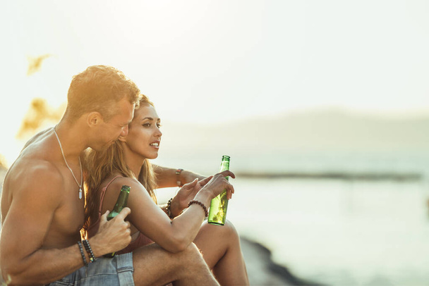Young couple having fun and drinking beer on the beach by the sea. Enjoying their love. - Foto, immagini