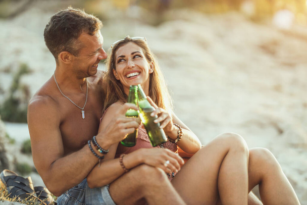Young couple enjoying their love and drinking beer on the beach by the sea. - Foto, Imagem