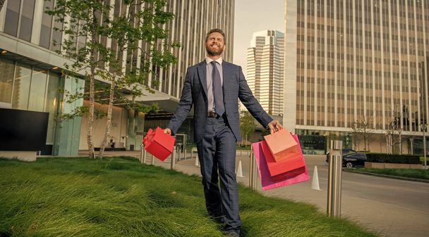 уверенный предприниматель в деловом костюме с сумкой и подарочной коробкой за пределами офиса, скидка. - Фото, изображение