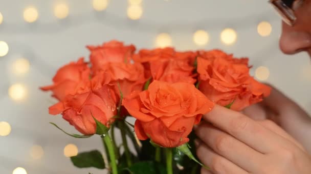 Kısa saçlı, mutlu bir kadın elinde bir buket kırmızı gülle oturuyor. Kız çiçeklere hafifçe dokunur ve kokularını koklar. Hediye. Doğum günün kutlu olsun. Mutlu Kadın Günü. - Video, Çekim