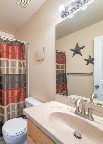 Vertikal Traditionelles kleines Badezimmer mit Satin-Duschvorhang. Es gibt ein Waschbecken mit Granitplatte und Spiegel in der Nähe der Toilette über die Sterne Ornamente und Handtuchhalter. - Foto, Bild