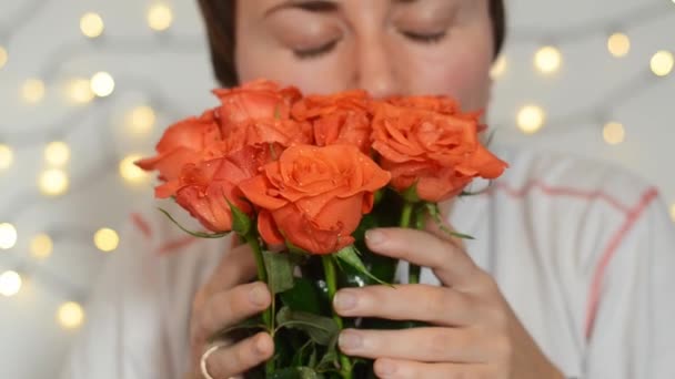 Kısa saçlı, mutlu bir kadın elinde bir buket kırmızı gülle oturuyor. Kız çiçeklere hafifçe dokunur ve kokularını koklar. Hediye. Doğum günün kutlu olsun. Mutlu Kadın Günü. - Video, Çekim