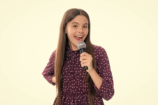 Teenage girl with microphone singing against white background with funny face. Singing lovely singer girl hold microphone. Portrait of happy smiling teenage child girl - Photo, Image