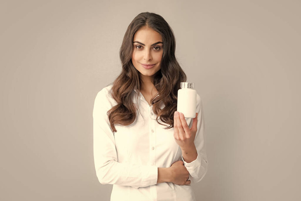 Femme avec des pilules de bouteille produit. Fille tenir supplément pilule bouteille isolé sur fond gris - Photo, image