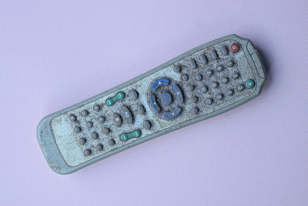 один старий сірий брудний пластиковий телевізійний пульт дистанційного керування з кольоровими кнопками лежить на бузковому столі
 - Фото, зображення