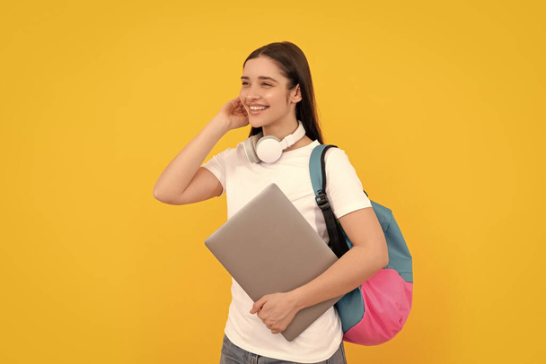 χαρούμενο νεαρό κορίτσι με σακίδιο κρατήσει φορητό υπολογιστή σε ακουστικά σε κίτρινο φόντο, e-learning. - Φωτογραφία, εικόνα