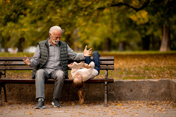Hezký dědeček tráví čas se svou vnučkou na lavičce v parku na podzim - Fotografie, Obrázek