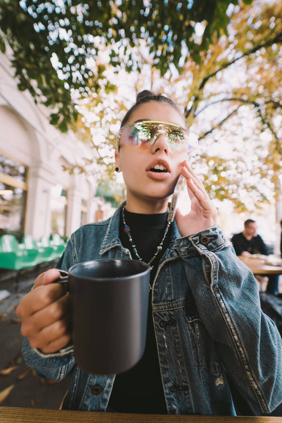 Fiatal nő hívja okostelefon és ital a városi utcai kávézó teraszán - Fotó, kép