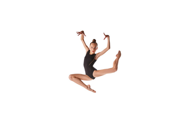 Jumping. Emotions in motion. Portrait of junior gymnast in black sport swimsuit doing gymnastics excercises isolated over white background. Sport, skills, achievements - Foto, Bild