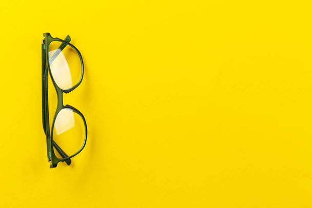 Stijlvolle brillen over gele achtergrond. Optische winkel, bril selectie, oogtest, visie onderzoek bij opticien, mode accessoires concept. Ruimte voor tekst. - Foto, afbeelding