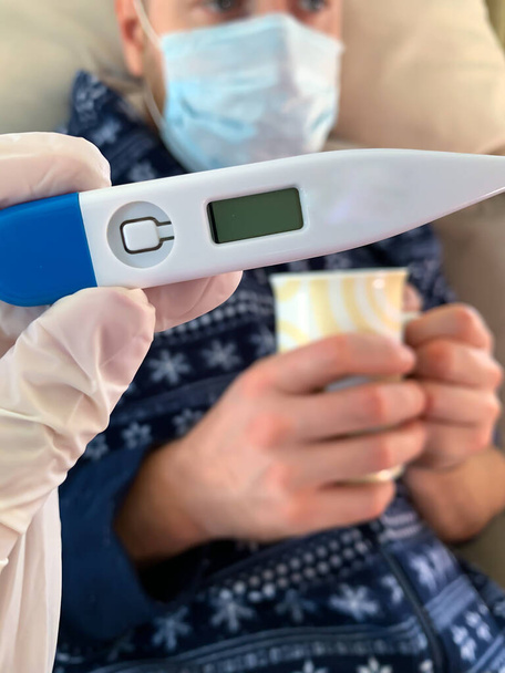 El guante médico sostiene un termómetro digital. Hombre enfermo. - Foto, imagen