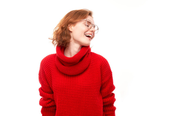 Portrait of positive redhead girl in red Christmas sweater emotionally rejoices and feels happy isolated on white background, advertising banner - Fotó, kép