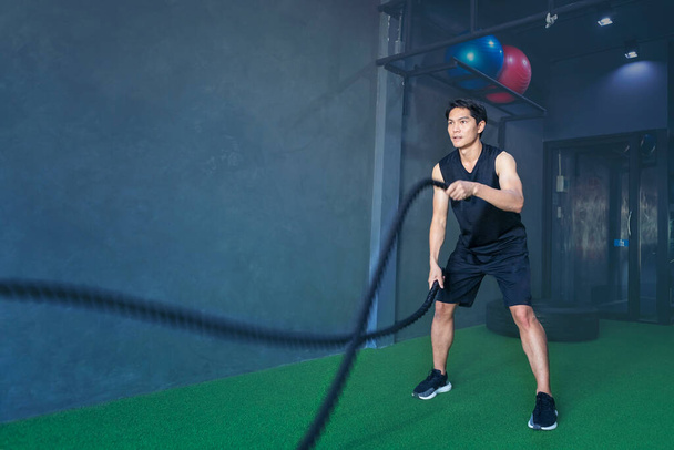 Man wearing a tank top to exercise at the gym with battle ropes - Photo, Image