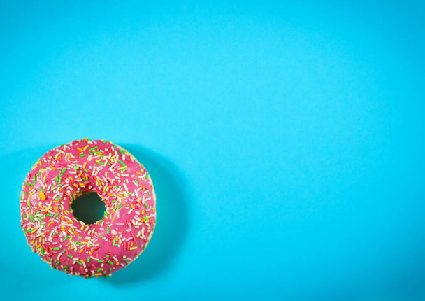 Perfect donut with pink icing and sprinkles on blue background. Studio shot, top view - Фото, зображення