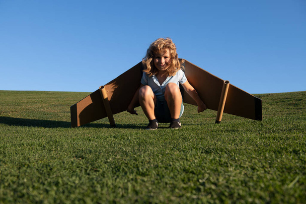 Kinderpiloot spelen met speelgoed vliegtuig vleugels in de zomer park. Innovatietechnologie en succesconcept. Kid piloot heeft plezier op gras in het park - Foto, afbeelding