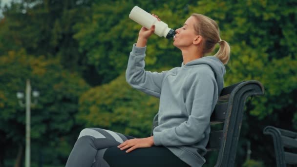 Dehydrated female sportswoman athlete girl tired runner jogger quench thirst after sport exercises in city park drink fresh cold water healthy sports nutrition refreshment health care body hydration - Footage, Video