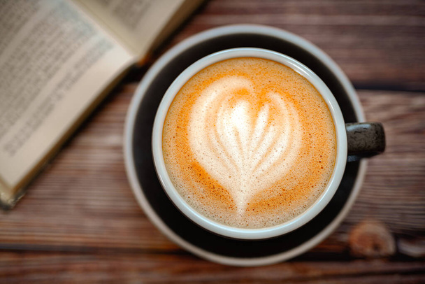 Une tasse de café d'art au lait de soja chaud sur une table en bois avec un livre dans un café  - Photo, image
