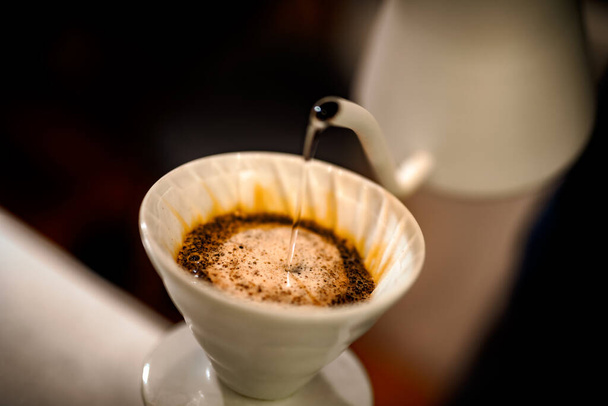 barista gieten warm water op ruwe bruine bubbels koffie door druppelfilter, home brewing proces - Foto, afbeelding