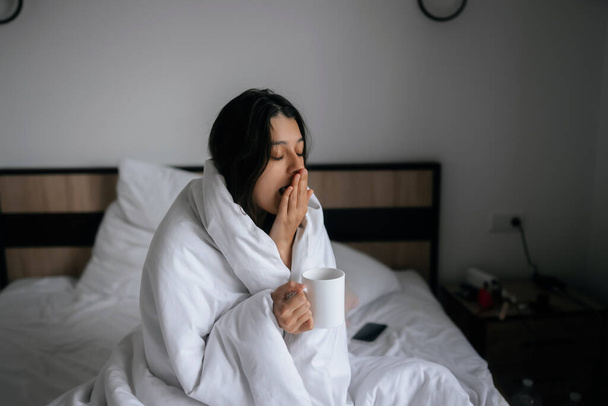 Bir kadın battaniyeye sarılmış ve uyandıktan sonra bir kupa tutuyor, bir gün mutlu ve rahat bir şekilde içeri giriyor iyi geceler uykusundan sonra. - Fotoğraf, Görsel