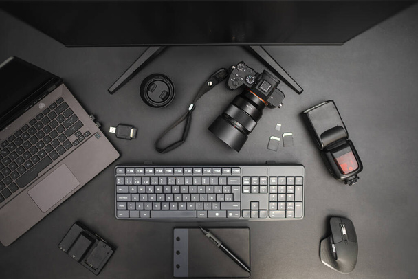 Рабочий стол на темном фоне с ноутбуком, фотоаппаратом, вспышкой, линзами, планшетом для рисования, клавиатурой, мышью. Вид сверху - Фото, изображение