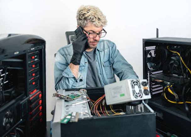 Caucasian man talking on the phone while repairing computer. White background - Фото, зображення