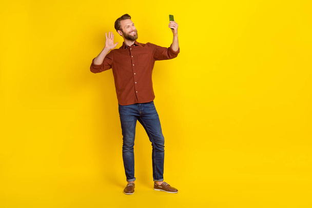 Full size photo of positive nice person hold telephone make selfie arm palm waving hi isolated on yellow color background. - Foto, Imagem
