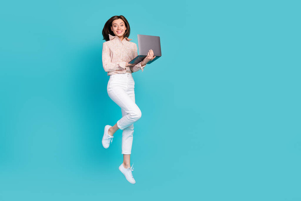 Full length photo of young carefree pretty business lady jumping air trampoline hold netbook empty space ad new job freelancer isolated on blue color background. - 写真・画像