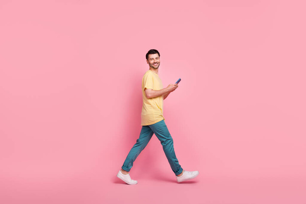 Full length profile side photo of good looking cheerful man go empty space read twitter facebook isolated on pink color background. - Foto, Bild