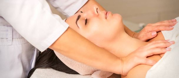 Молодая белая женщина с закрытыми глазами получает массаж груди в клинике красоты - Фото, изображение