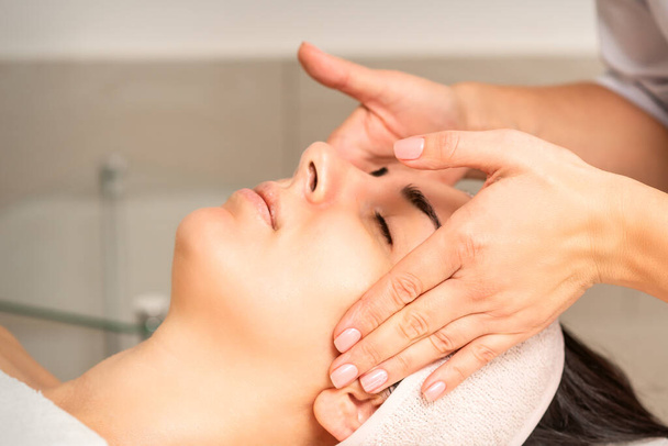 Jovem caucasiana com olhos fechados recebendo uma massagem facial em uma clínica de beleza - Foto, Imagem