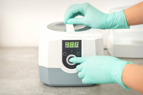 Kosmetyk w rękawiczkach ochronnych uruchamia maszynę do dezynfekcji narzędzi przed zabiegiem medycznym - Zdjęcie, obraz