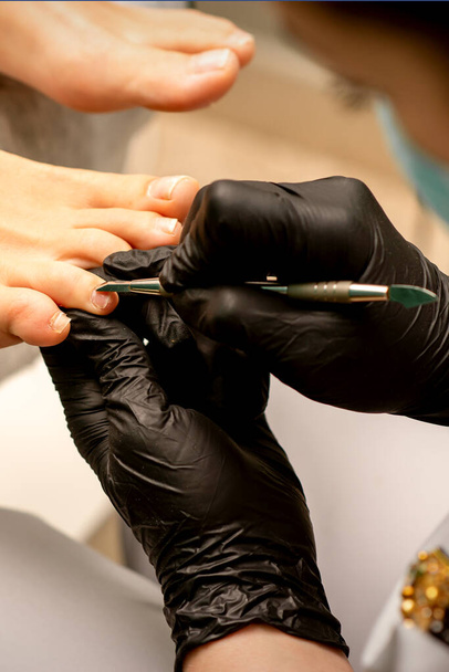 Professionelle Pediküre. Prozess der Nagelhautentfernung an weiblichen Zehen im Wellness-Salon. Schönheitsbegriff - Foto, Bild