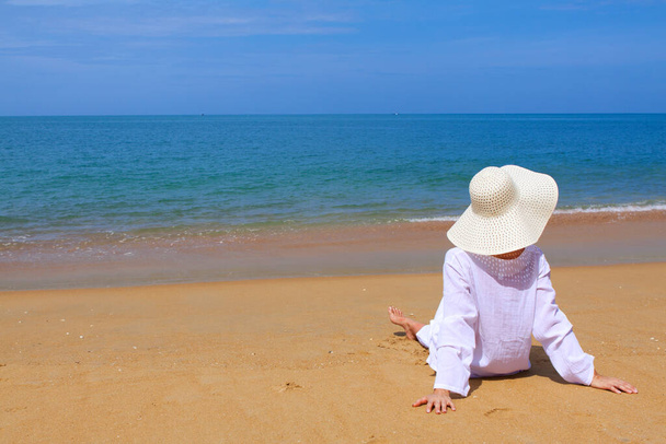 festői lövés fiatal nő fehér ruhák és kalap időt töltenek a strandon nyaralás közben - Fotó, kép