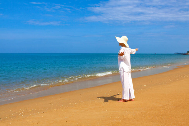 schilderachtig schot van jonge vrouw met witte kleren en hoed tijd doorbrengen op het strand tijdens vakantie - Foto, afbeelding