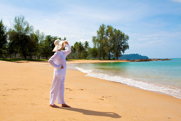 schilderachtig schot van jonge vrouw met witte kleren en hoed tijd doorbrengen op het strand tijdens vakantie - Foto, afbeelding